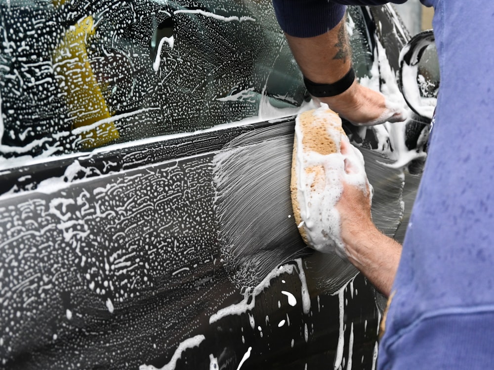 Foam-covered mitt being drawn across a wet car panel by hand